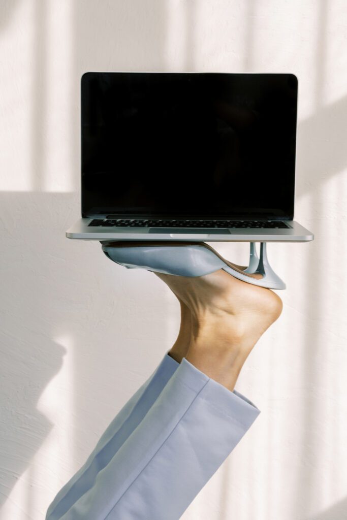 Creative business concept — woman balancing laptop on high heel, modern workspace aesthetic